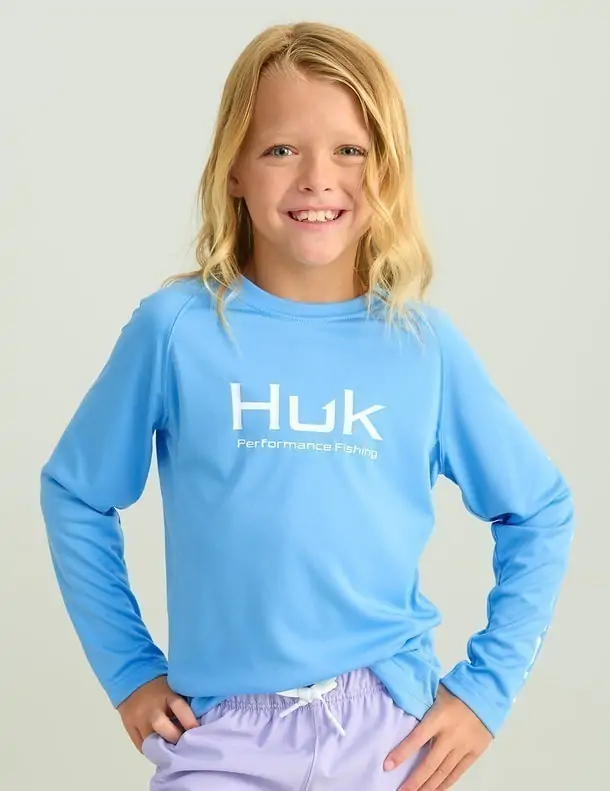 Girl wearing a blue Huk long-sleeve performance shirt, designed for sun protection during coastal activities in 30A.